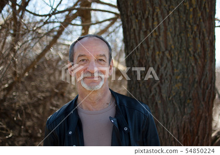 Male portrait of mature senior man with grey hair and beard in dark leather jacket standing outdoors 54850224
