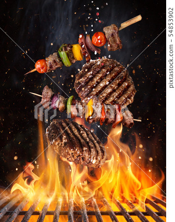 Tasty beef steaks and skewers flying above cast iron grate with fire flames. 54853902