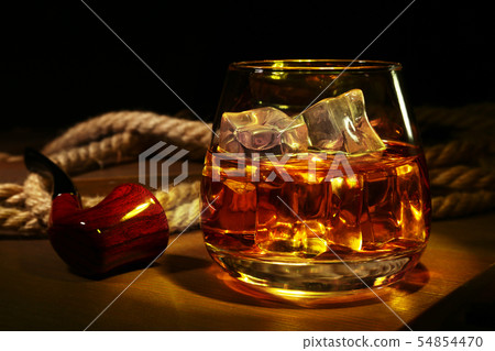 Glass with whiskey, ice cubes and smoking pipe on wooden background. 54854470