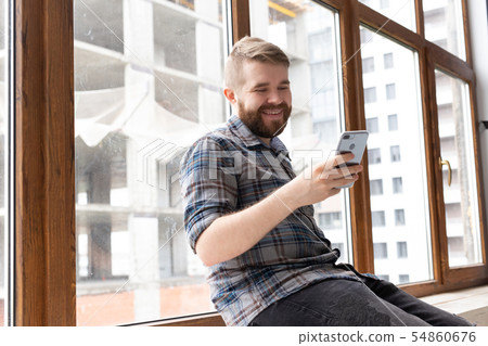 Cute young hipster guy with stylish clothes is sitting on social networks using a smartphone and 54860676