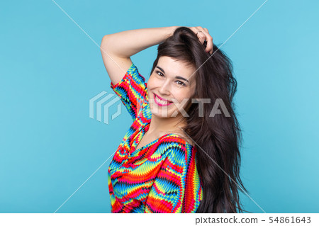 Cheerful young brunette woman with long hair posing on a blue background with copy space. The Cheerful young brunette woman with long hair posing on a blue background with copy space. The 54861643