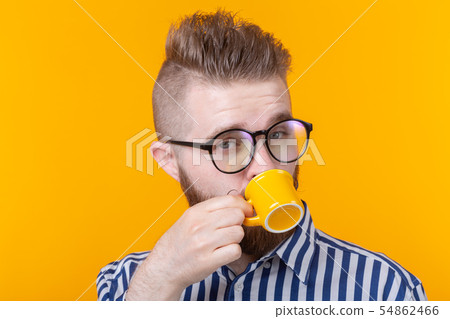 Cute confident young man drinking coffee from a little yellow mug while standing against a yellow Cute confident young man drinking coffee from a little yellow mug while standing against a yellow 54862466