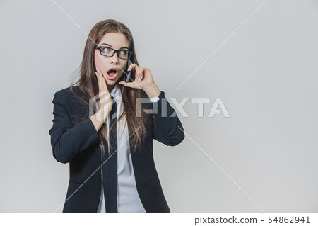 Shocked pretty businesswoman is holding a phone in her hand and talking. Attractive lady is looking Shocked pretty businesswoman is holding a phone in her hand and talking. Attractive lady is looking 54862941