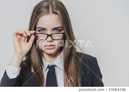 Close up portrait of a serious businesswoman, who is touching the black rim of glasses with one hand Close up portrait of a serious businesswoman, who is touching the black rim of glasses with one hand 54864386