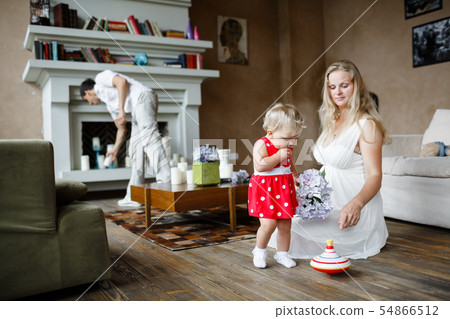 Pregnant woman in white dress playing with one year old baby sitting on a floor 54866512