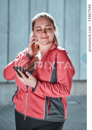 Enjoying workout. Happy plus size woman in headphones holding smart phone and listening music with Enjoying workout. Happy plus size woman in headphones holding smart phone and listening music with 54867946