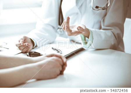 Doctor and female patient sitting at the desk and talking in clinic near window. Medicine and health Doctor and female patient sitting at the desk and talking in clinic near window. Medicine and health 54872456