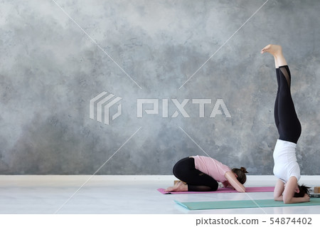 Women standing in salamba sirsasana exercise and balasana Women standing in salamba sirsasana exercise and balasana 54874402