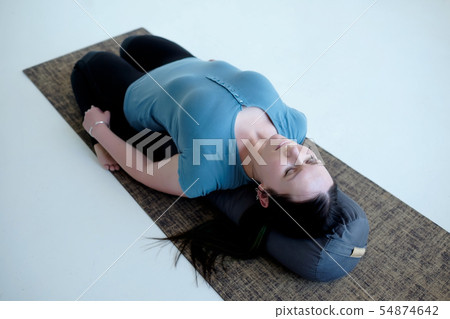 Cauacasian woman resting in reclining hero pose or Supta Virasana with bolster 54874642
