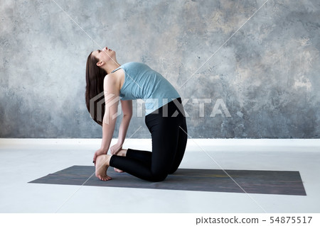 Woman practicing yoga, doing Ushtrasana, Camel Pose, at studio full length. 54875517