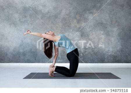 Woman practicing yoga, doing Ushtrasana, Camel Pose, at studio full length. 54875518