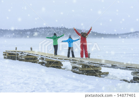 Three girls of different ages and height in colorful winter suits with snowflakes on nature on a Three girls of different ages and height in colorful winter suits with snowflakes on nature on a 54877401