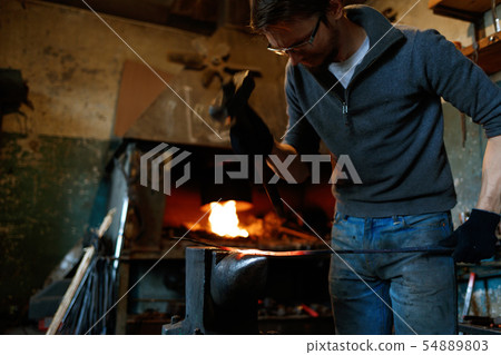 Blacksmith forging red-hot metal with hammer. 54889803