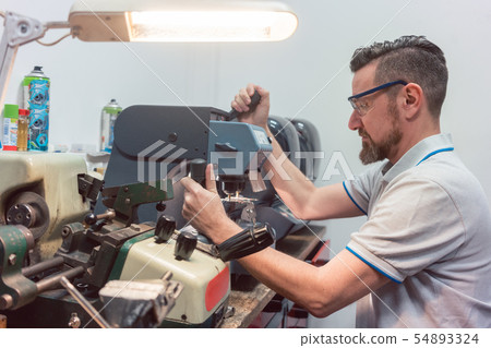 Locksmith cutting key with his machine 54893324