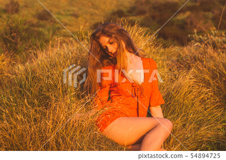 Young blonde girl in red dress sitting on grass Young blonde girl in red dress sitting on grass 54894725