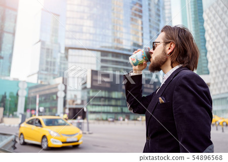 Photo on side of brunet with beard and earring in ear drinking from glass in city on background of Photo on side of brunet with beard and earring in ear drinking from glass in city on background of 54896568