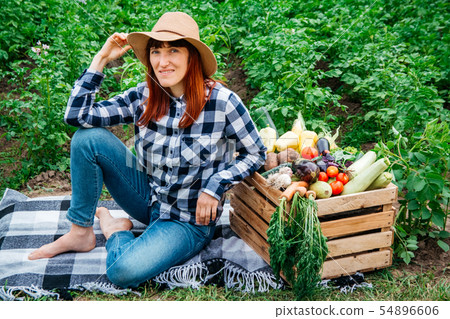 Beautiful female farmer sitting on a blanket near fresh organic vegetables in a wooden box against 54896606