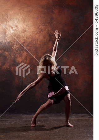 Full-length photo of dancing blonde girl looking in side in short black dress on dark brown Full-length photo of dancing blonde girl looking in side in short black dress on dark brown 54896608
