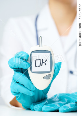 Photo of person’s hand in rubber gloves with glucometer with inscription ok at table with 54896672
