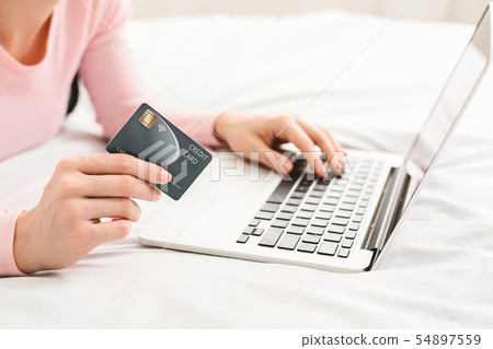 Woman using her credit card and laptop in bed 54897559