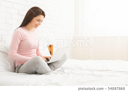 Woman sitting on bed and working on laptop 54897868