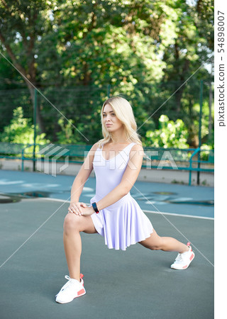 Young slim woman with a sporty body, long blond hair, dressed in a pink sports dress, performs an Young slim woman with a sporty body, long blond hair, dressed in a pink sports dress, performs an 54898007