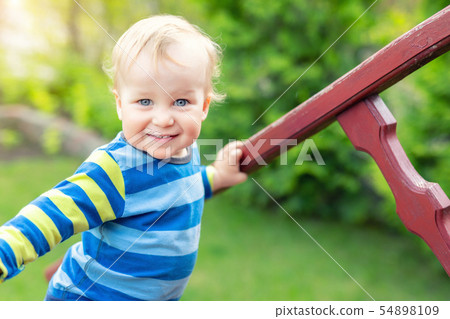 Portrait of cute mischievous caucasian blond baby boy holding wooden banister climbing staircase at Portrait of cute mischievous caucasian blond baby boy holding wooden banister climbing staircase at 54898109