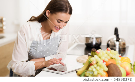 Millennial woman searching recipe on tablet, cooking dinner Millennial woman searching recipe on tablet, cooking dinner 54898378