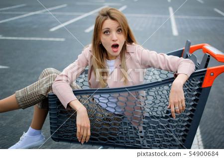 Young attractive girl in the parking lot of the supermarket climbed into the cart. Shopping concept. 54900684