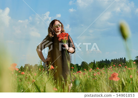 Plus sized woman in a black dress on a field of green wheat and wild poppies. Overweight fat woman. Plus sized woman in a black dress on a field of green wheat and wild poppies. Overweight fat woman. 54901853