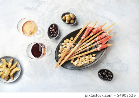 Italian antipasti. Grissini, prosciutto di parma, artichokes, olives, wine glasses, overhead shot 54902529