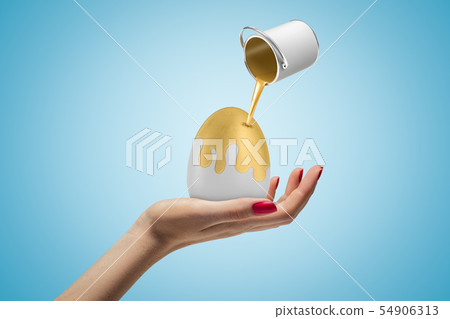Side closeup of woman's hand holding grey egg and little bucket of golden paint in air pouring paint Side closeup of woman's hand holding grey egg and little bucket of golden paint in air pouring paint 54906313