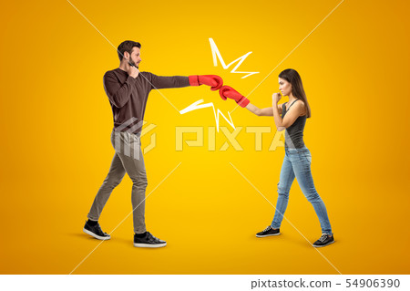 Young man and woman wearing casual clothes and boxing gloves fighting on yellow background Young man and woman wearing casual clothes and boxing gloves fighting on yellow background 54906390