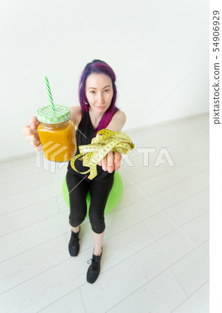 Blurry young hipster girl with colored hair holding a banana protein smoothie and measuring tape 54906929
