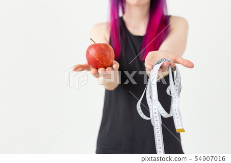 Young blurred asian girl hipster colored hair holding in hands a measuring tape and apple posing on Young blurred asian girl hipster colored hair holding in hands a measuring tape and apple posing on 54907016