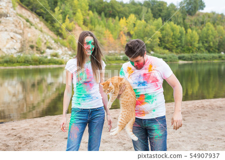Festival holi, tourism and nature concept - Portrait of woman and man with cat covered multi-colored Festival holi, tourism and nature concept - Portrait of woman and man with cat covered multi-colored 54907937