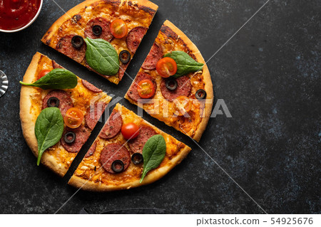 Cut into slices delicious fresh pizza with pepperoni on a dark background. Top view . Pizza on the 54925676