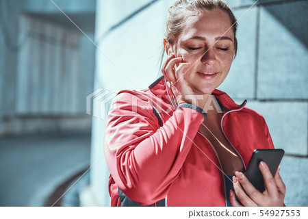 My favorite playlist. Happy plus size woman in headphones holding smart phone and listening music My favorite playlist. Happy plus size woman in headphones holding smart phone and listening music 54927553