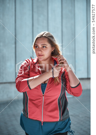 Healthy female. Vertical photo of pretty plus size woman in sport clothes adjusting her long hair Healthy female. Vertical photo of pretty plus size woman in sport clothes adjusting her long hair 54927577