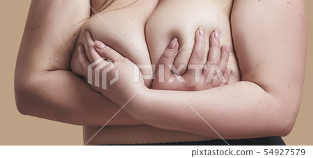 I love myself. Close up cropped photo of plus size naked woman holding her bust while standing 54927579