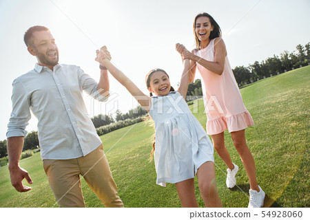 Let's play Full length of young and happy parents carrying their daughter and smiling while spending 54928060