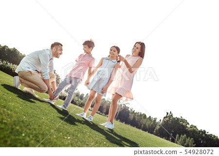 Attentive parents. Young parents are tying shoelaces and adjusting hair for their children while 54928072