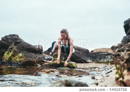 Woman in sportswear with prosthetic leg taking water in her hand from the river Woman in sportswear with prosthetic leg taking water in her hand from the river 54928788