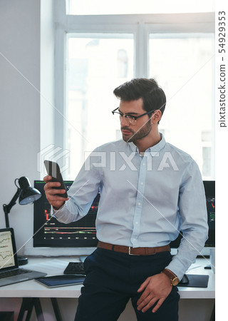 Successful businessman. Concentrated young trader in formal wear and eyeglasses is looking at Successful businessman. Concentrated young trader in formal wear and eyeglasses is looking at 54929353