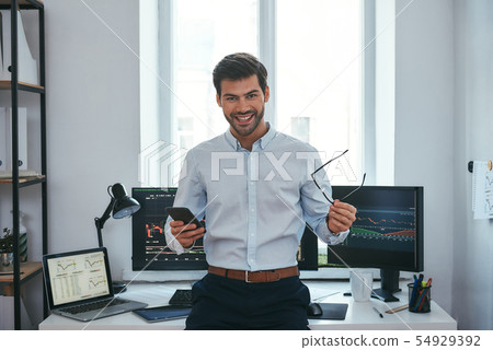 Great Happy young businessman or trader in formalwear holding eyeglasses and smartphone and smiling 54929392