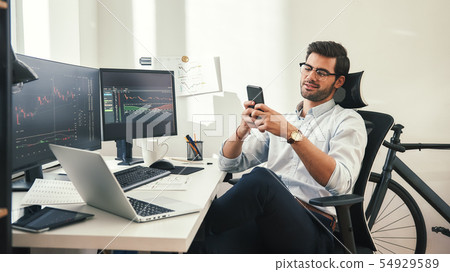 Using modern technologies. Relaxed young trader in formal wear and eyeglasses is using his Using modern technologies. Relaxed young trader in formal wear and eyeglasses is using his 54929589