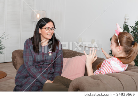 Mom and daughter are sitting on the couch and 54929669
