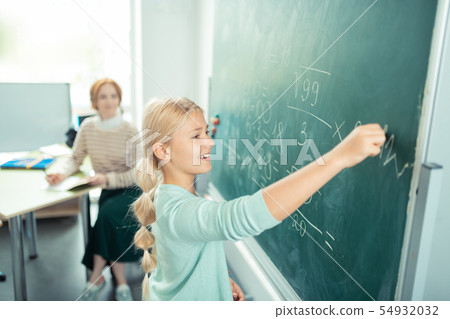 Happy girl doing sums near the school board. Happy girl doing sums near the school board. 54932032