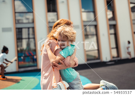 Smiling boy cuddling with his mom in the school yard. 54933537
