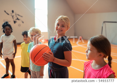 Smiling girl holding a ball standing next to her classmates. Smiling girl holding a ball standing next to her classmates. 54933777